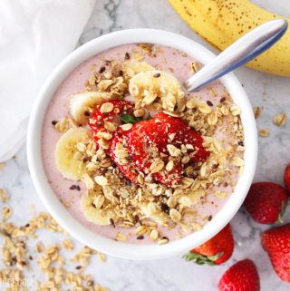smoothie bowl topped with fruit and granola on a marble counter top