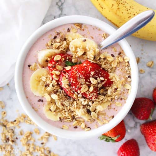 Smoothie bowl topped with fruit and granola on a marble counter top.
