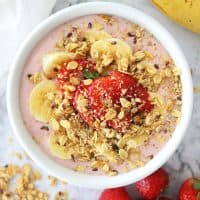 Strawberry smoothie bowl in a white bowl topped with fresh fruit and granola