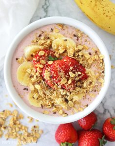 Strawberry smoothie bowl in a white bowl topped with fresh fruit and granola