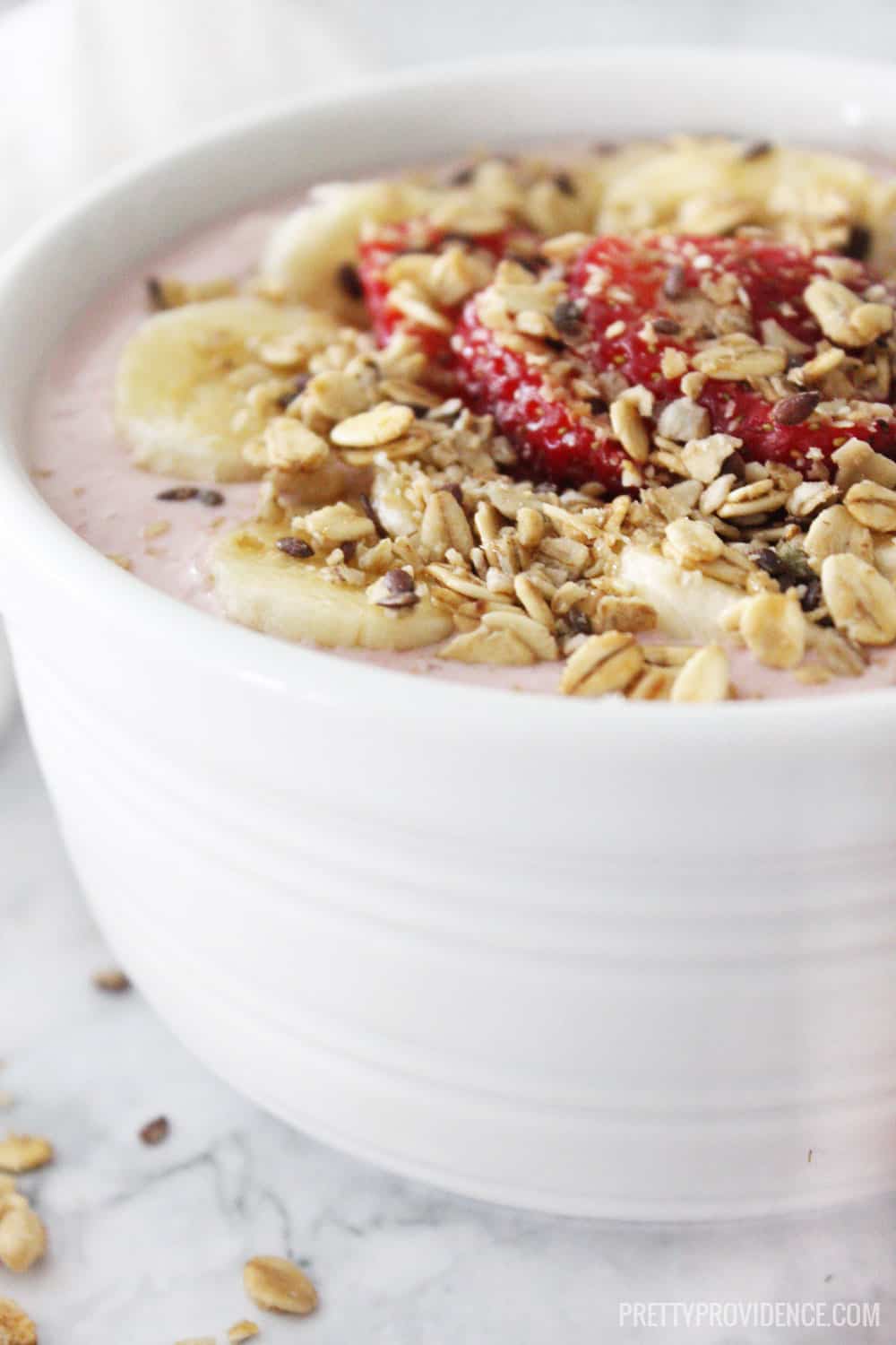 strawberry smoothie in white bowl topped with banana, strawberries, and granola