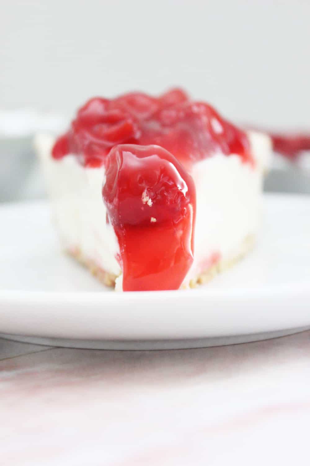 looking straight on the point of a slice of cream cheese pie on a white plate with cherry pie filling on top