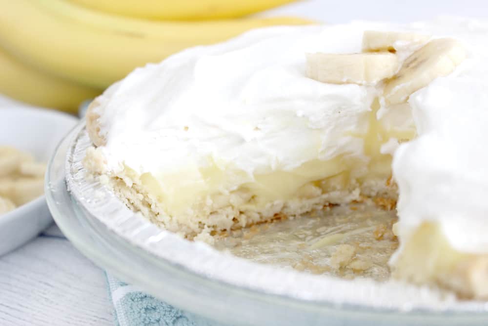 banana cream pie with a slice missing. bananas in the background