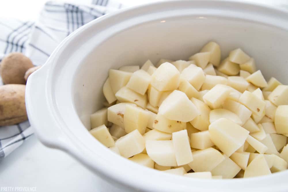 Peeled and chopped potatoes in a white slow cooker bowl.