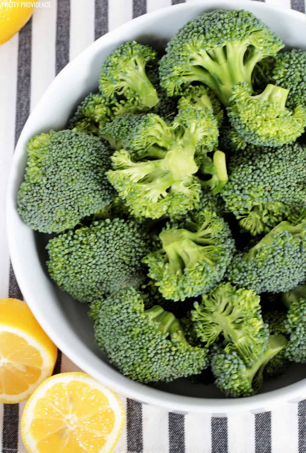 a white bowl full of raw broccoli on a white and grey striped background