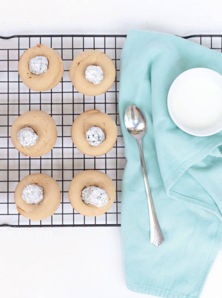 Cake donuts on a cooling rack with tin foil cylinders in the middle, just out of the oven.