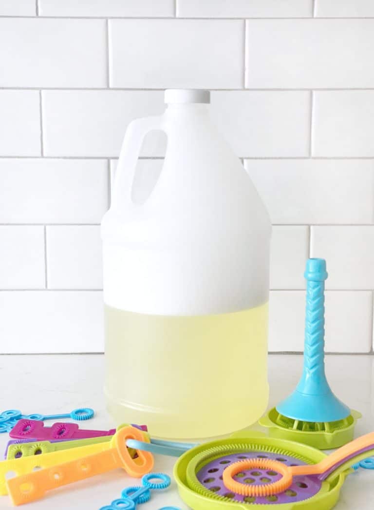 homemade bubble solution in a white gallon jug with wands in front of it