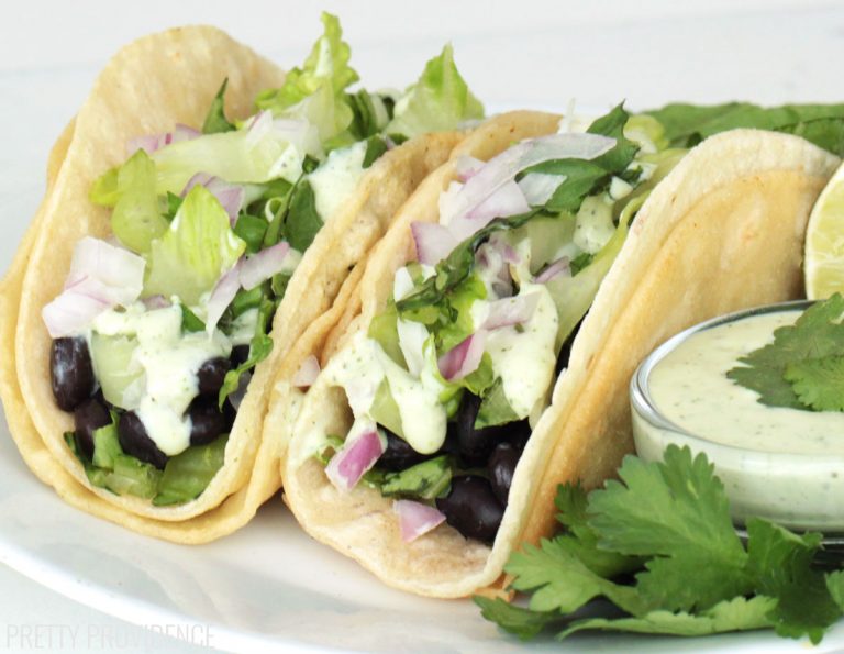 Black bean tacos on corn tortillas topped with lettuce, red onion, jalapeño ranch