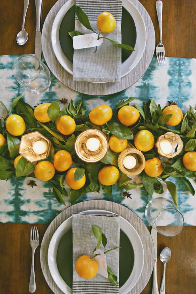 Thanksgiving table setting. Shibori table runner blue and white, with orange citrus fruit and leaves, and black plates with gray napkins.
