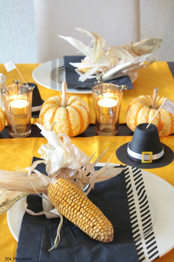 Thanksgiving table: pilgrim's hat place card holders, orange pumpkins and black napkins with corn and husks on the plates.