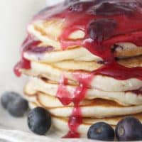 A stack of blueberry pancakes with blueberry syrup dripping down.