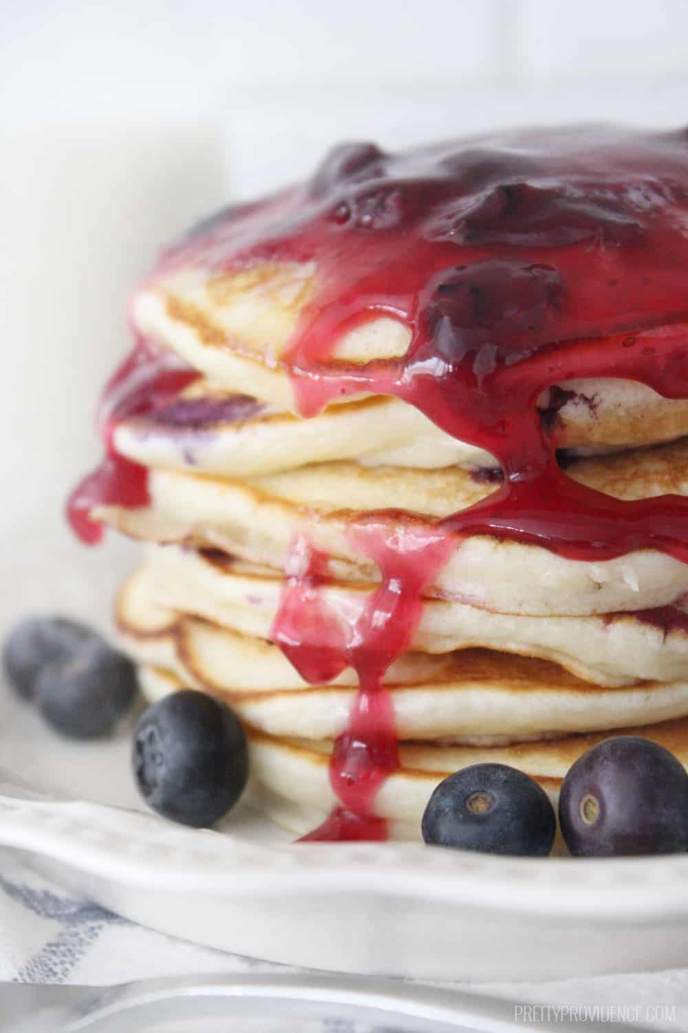 A stack of blueberry pancakes with blueberry syrup dripping down.