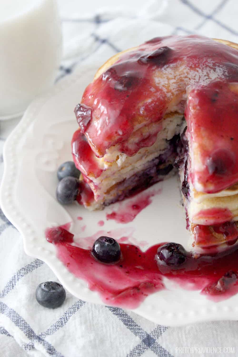 A stack of blueberry pancakes with blueberry syrup and a wedge shape cut out. 