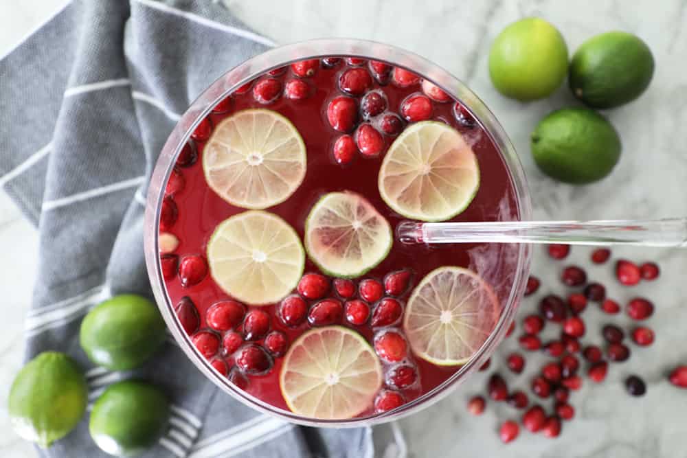 cranberry punch in punchbowl by black tea towel with fresh limes and cranberries surrounding