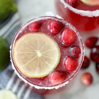 cranberry punch in a sugared glass surrounded by a tea towel, limes and cranberries