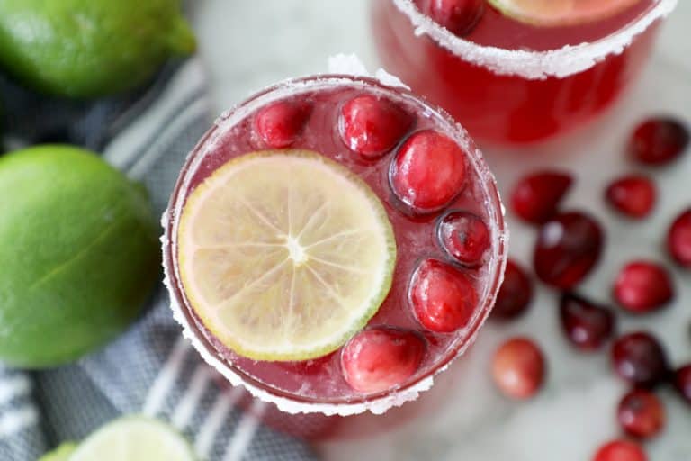 cranberry punch in a sugared glass surrounded by a tea towel, limes and cranberries