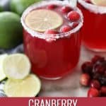 a glass of cranberry punch on a marble counter by fresh limes and cranberries