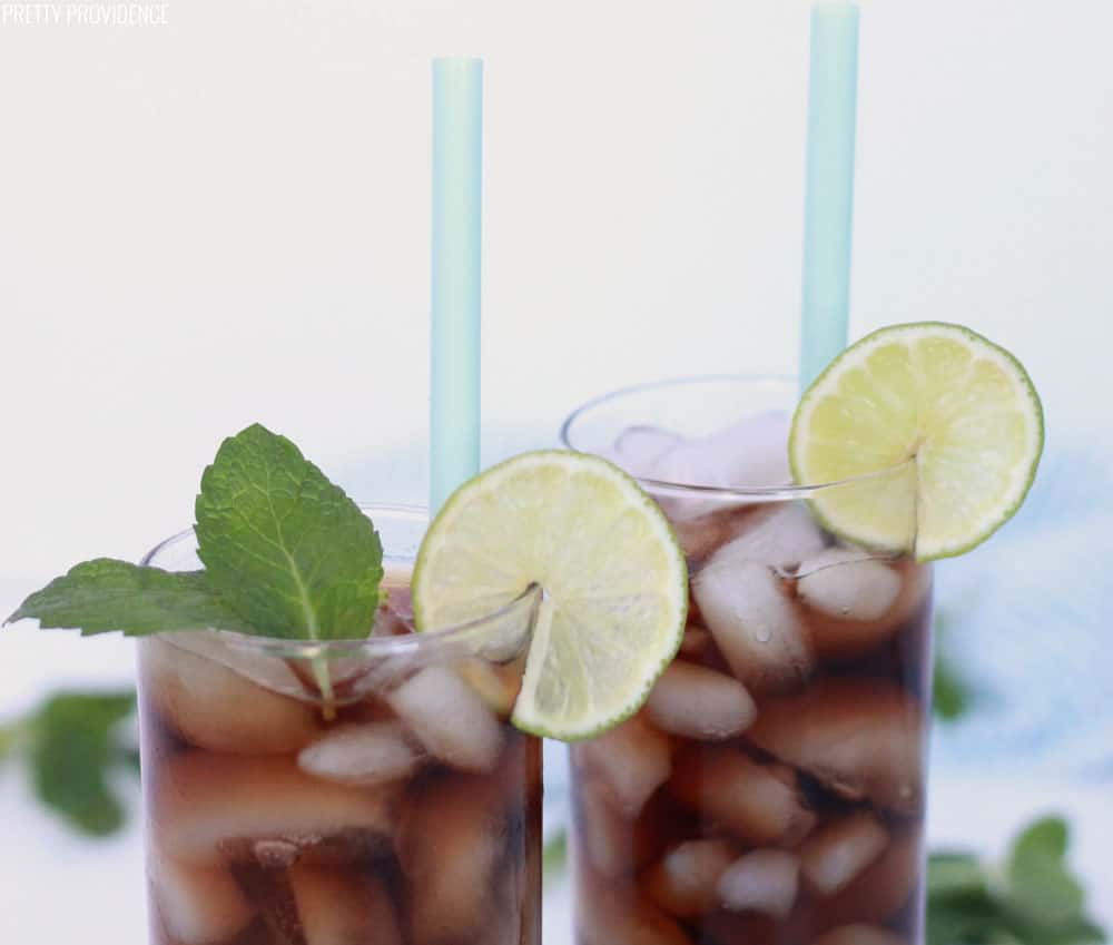 Dirty Dr. Pepper drink with coconut and lime in clear glasses with lime slices and fresh mint as garnish.