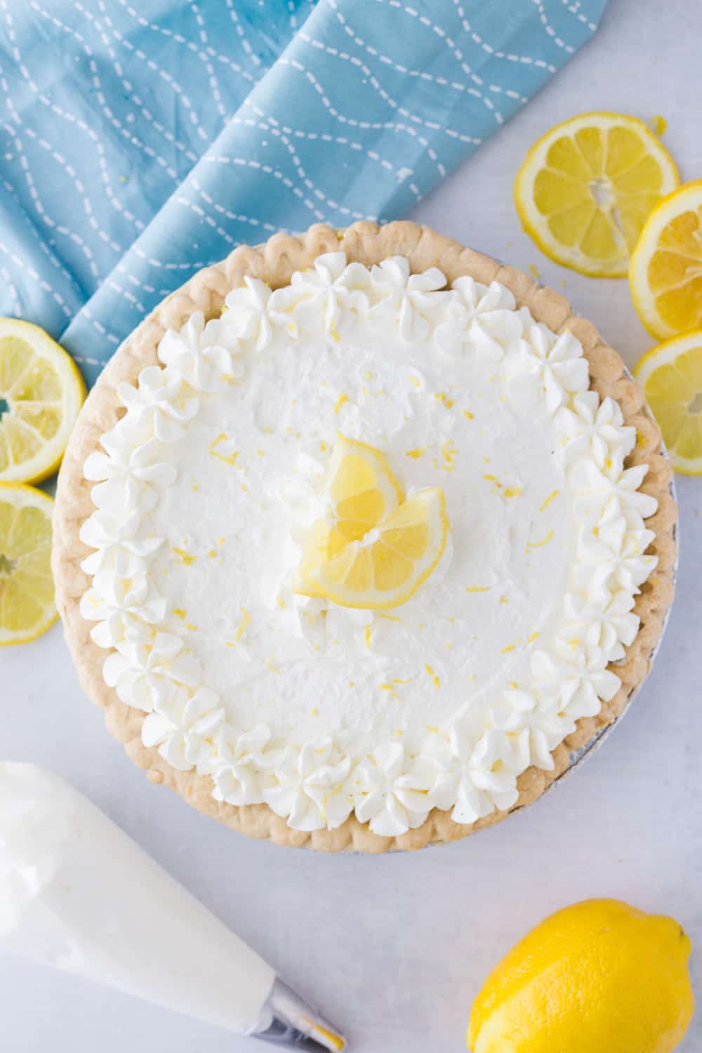 birds eye view of a lemon sour cream pie next to some sliced lemons and a whipped cream piper