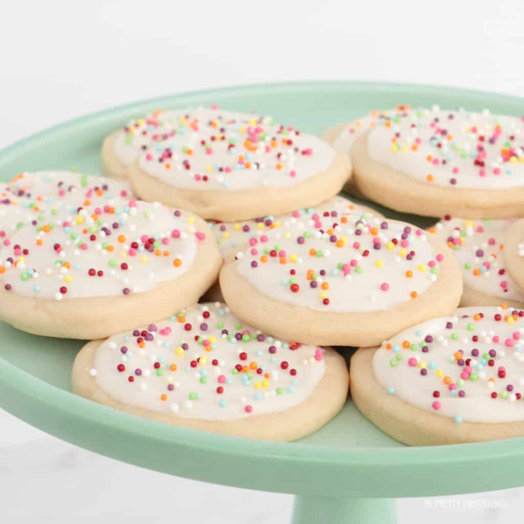 Soft sugar cookies with white frosting and sprinkles on green cake stand