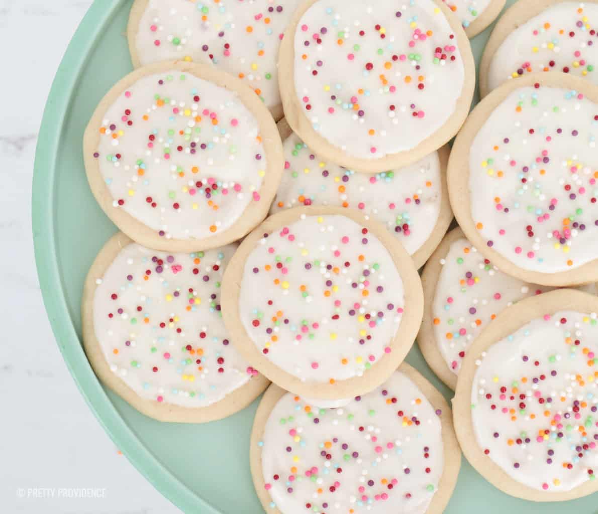 Homemade sugar cookies with cream cheese frosting and sprinkles on a jade plate