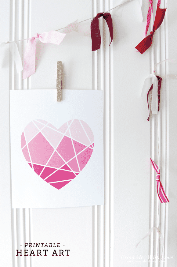 Geometric heart with light pink sections on top, medium pink in the middle and dark pink at the bottom, hung up on a white wall with a clothes pin.