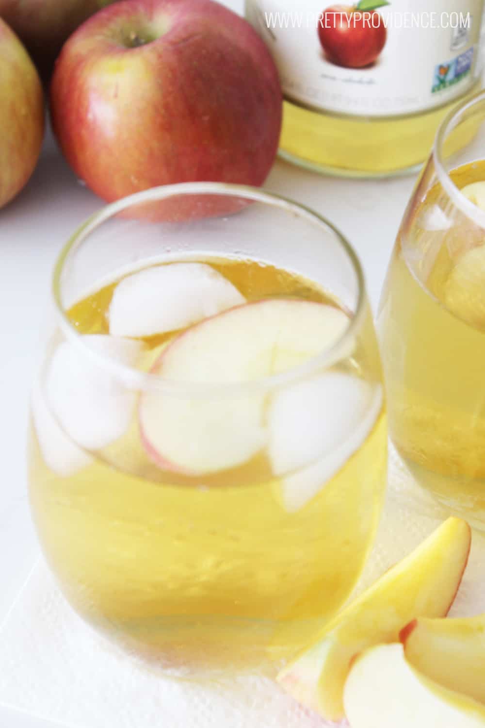 stemless wine glass with ice and sparkling cider, apples and bottom of bottle in background