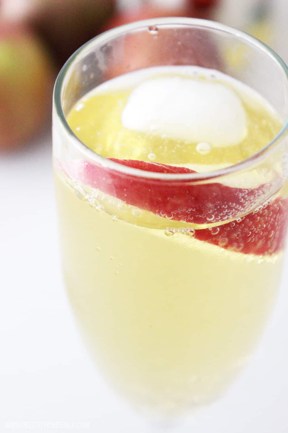 close up view of a glass of sparkling apple cider with apple slice to garnish