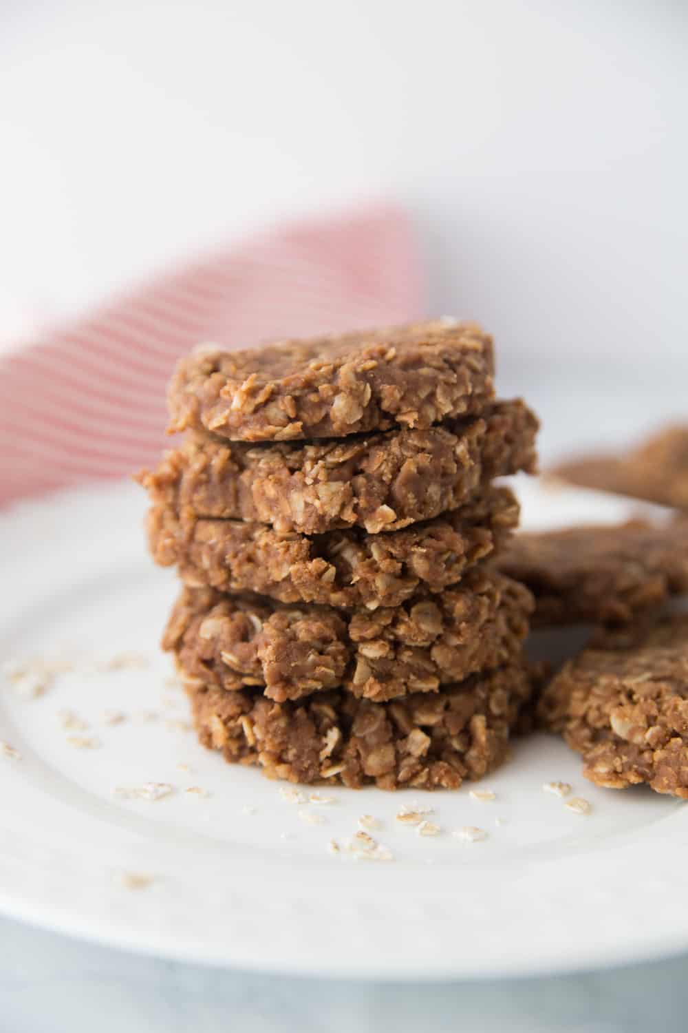 five no bake cookies stacked on a white plate with oats sprinkled around