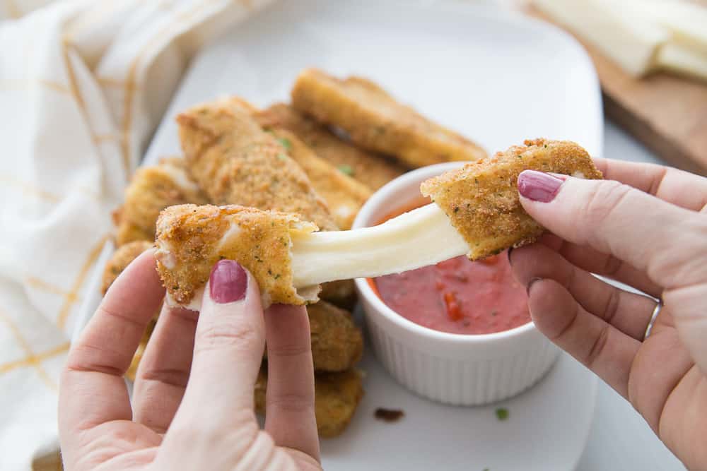 a cheese stick being pulled apart from both edges showing melty cheese in the middle