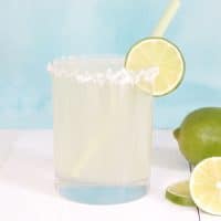Coconut Limeade in a glass with shredded coconut and a lime slice on the rim, and sliced limes on the side.