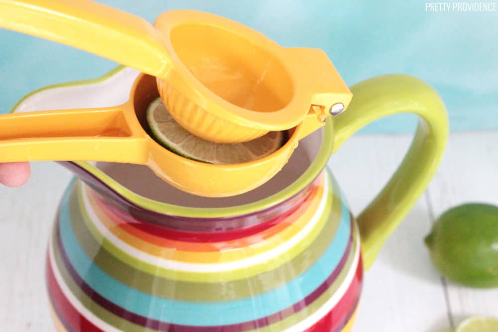 Citrus squeezer with a lime in it, being squeezed over a colorful pitcher.