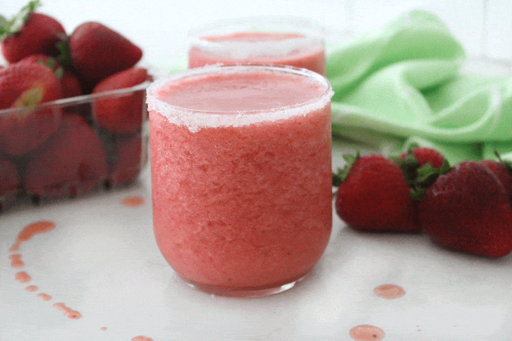 Strawberry slush in a sugar rimmed glass with strawberries and a green cloth