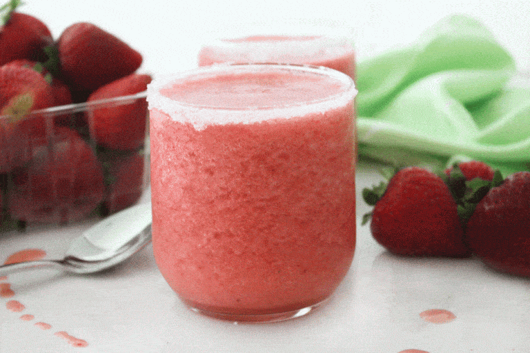 strawberry slush with a silver spoon, green cloth and strawberries around it