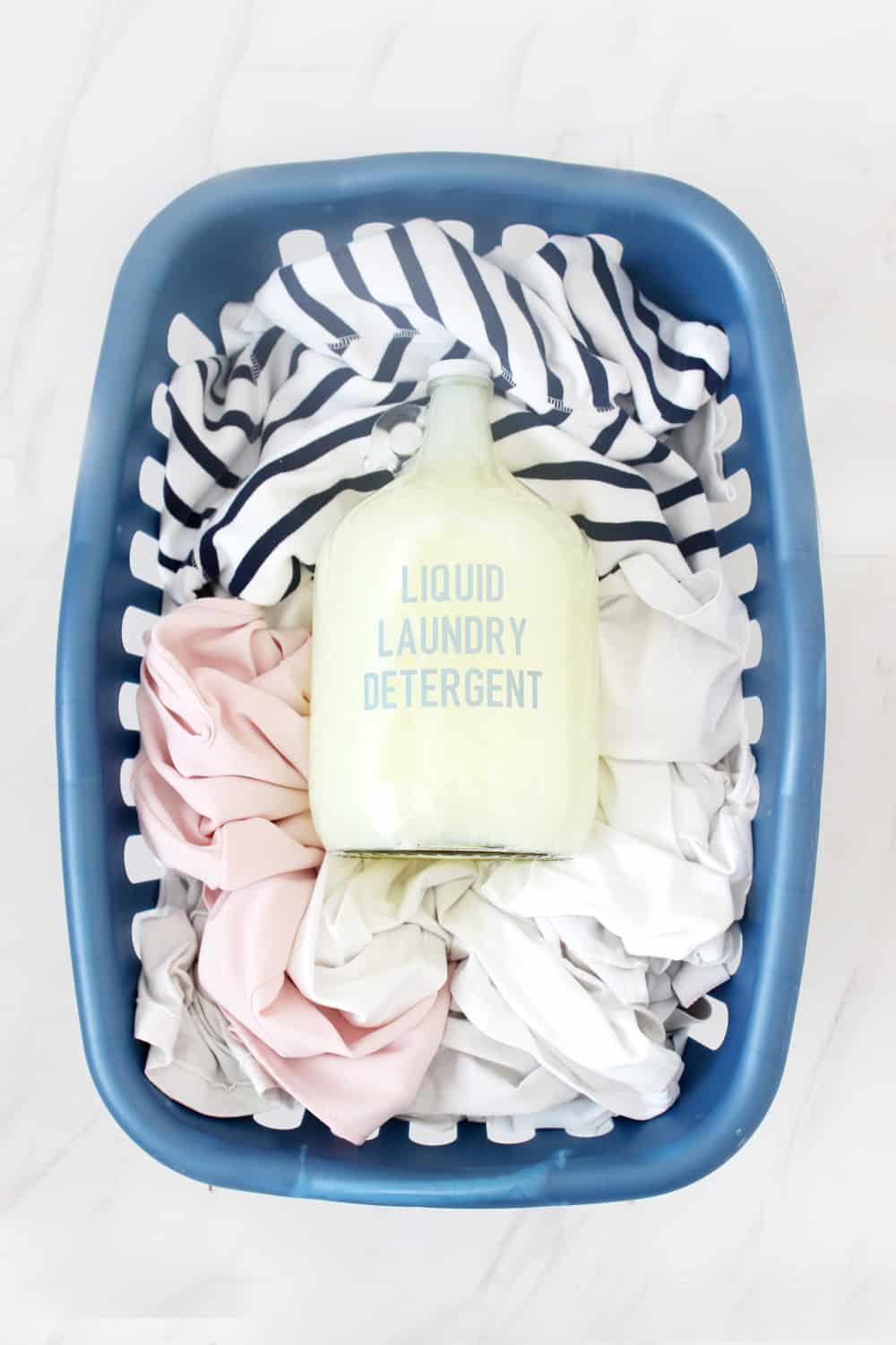 gallon jug of diy liquid laundry detergent in a blue laundry hamper filled with clothes