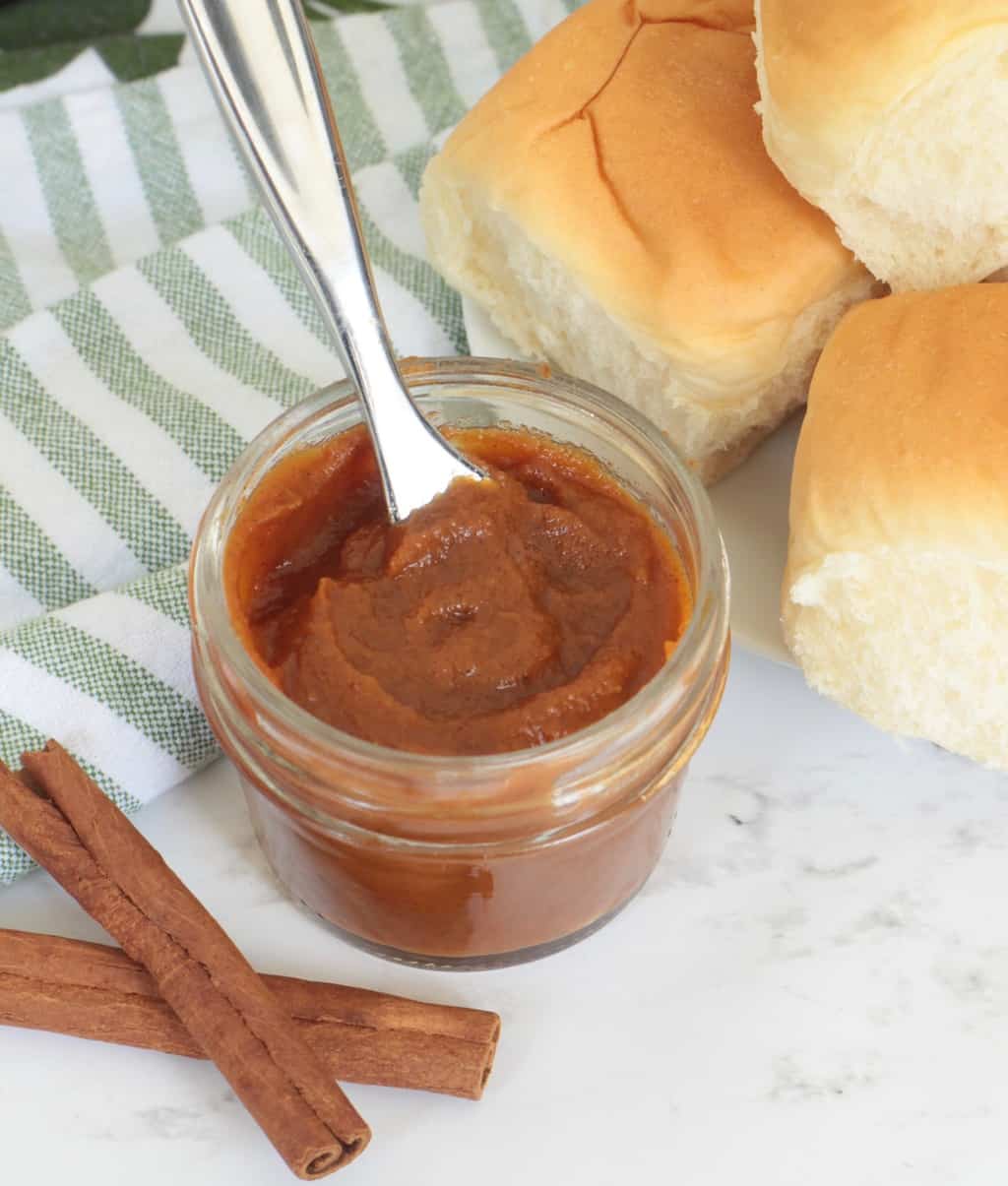 Pumpkin Butter Homemade in the Slow Cooker, in a small baby food jar with fresh rolls and cinnamon sticks next to it.