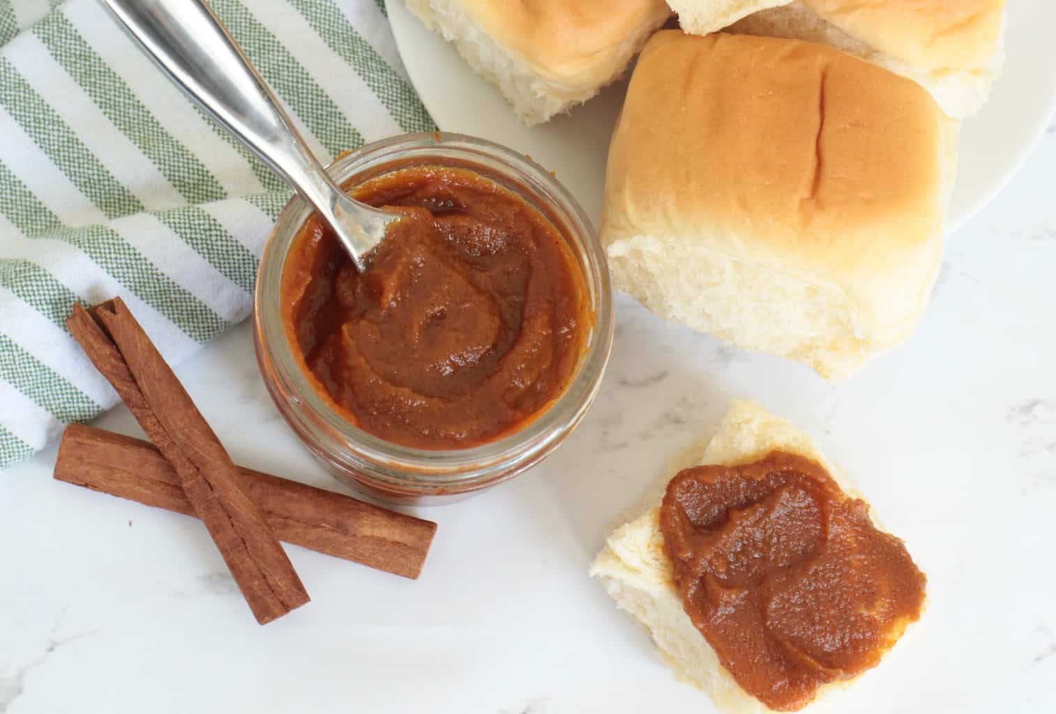 Homemade Pumpkin Butter in a small jar, some spread on a freshly baked roll.
