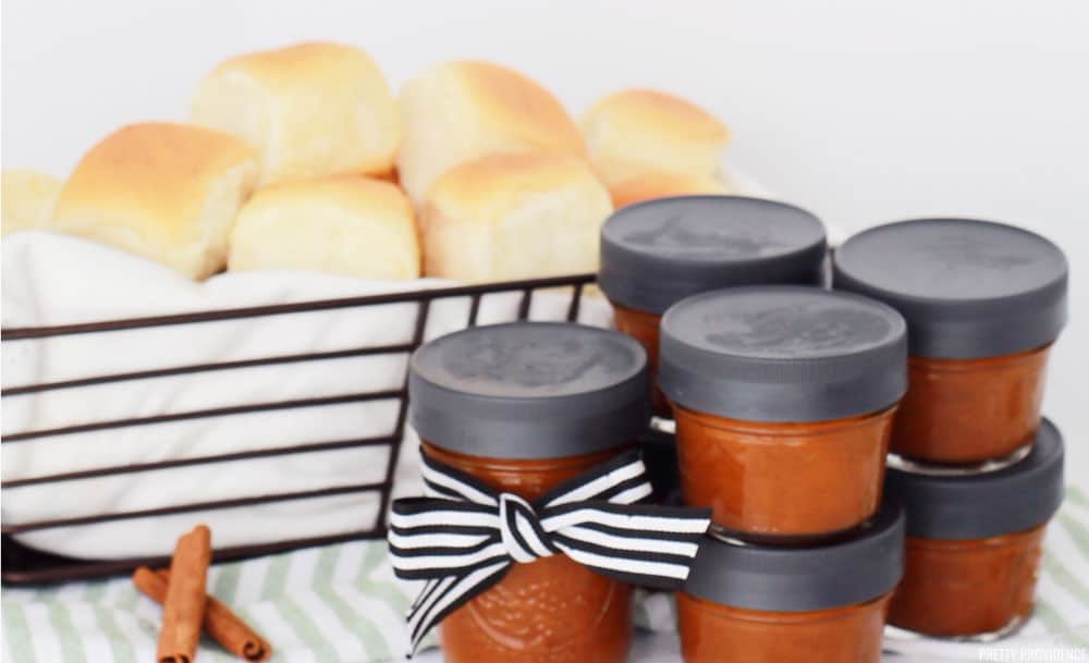 Pumpkin Butter homemade in small baby food jars stacked next to a bread basket full of fresh rolls.