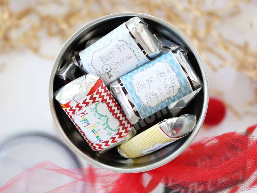 birds eye view of a tumbler filled with mini candy bars on a white counter next to red ribbon and brown crinkle paper