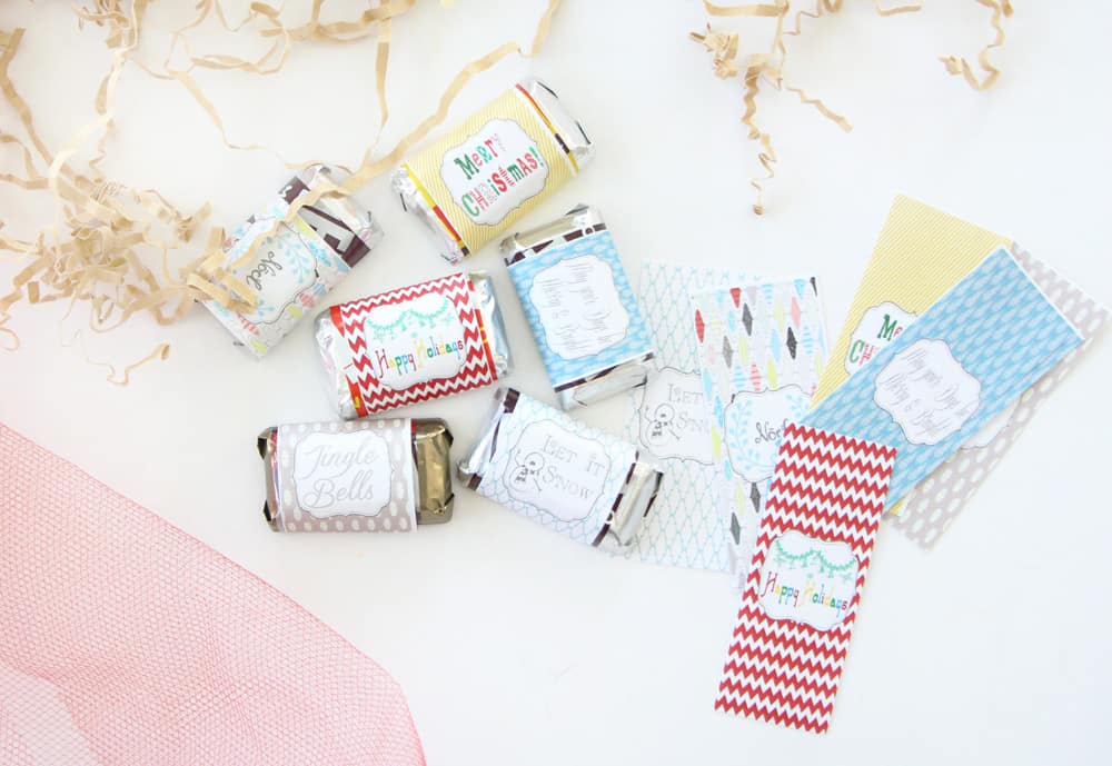 christmas candy bar wrappers next to mini wrapped candy bars on a white counter with red ribbon and brown crinkle papers