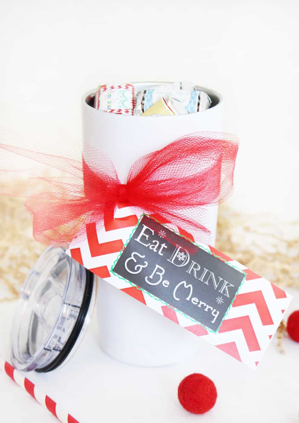 white tumbler with Christmas tag and red ribbon against a white background