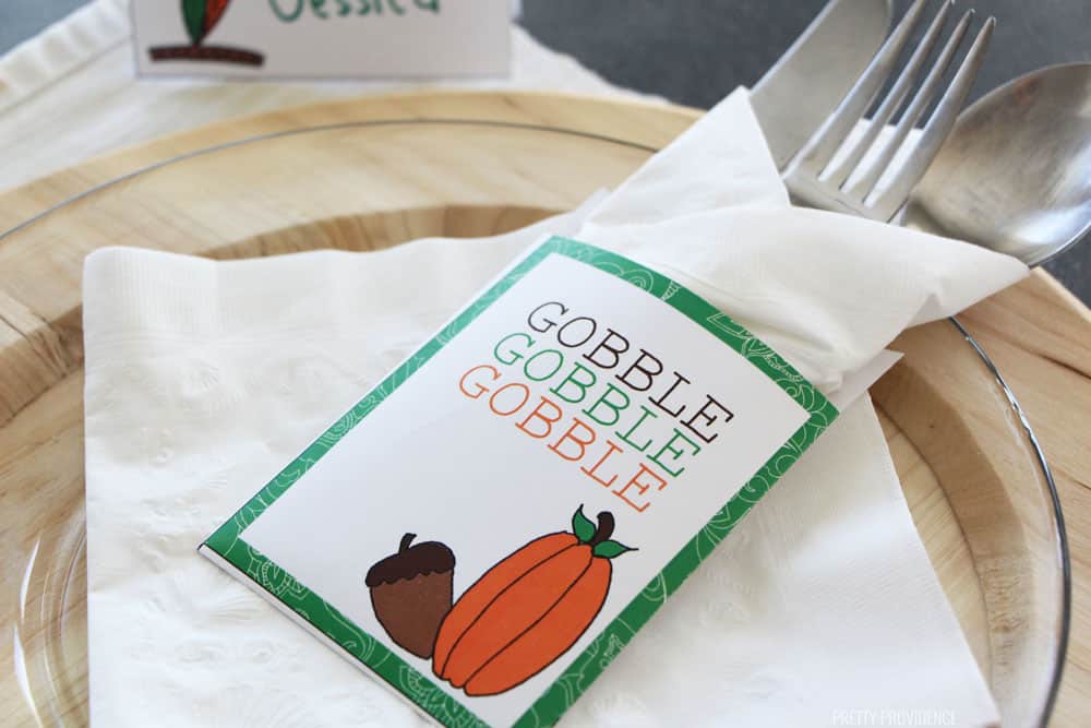 Free Thanksgiving Printable Utensil Holder on a white napkin, clear plate and wood charger.