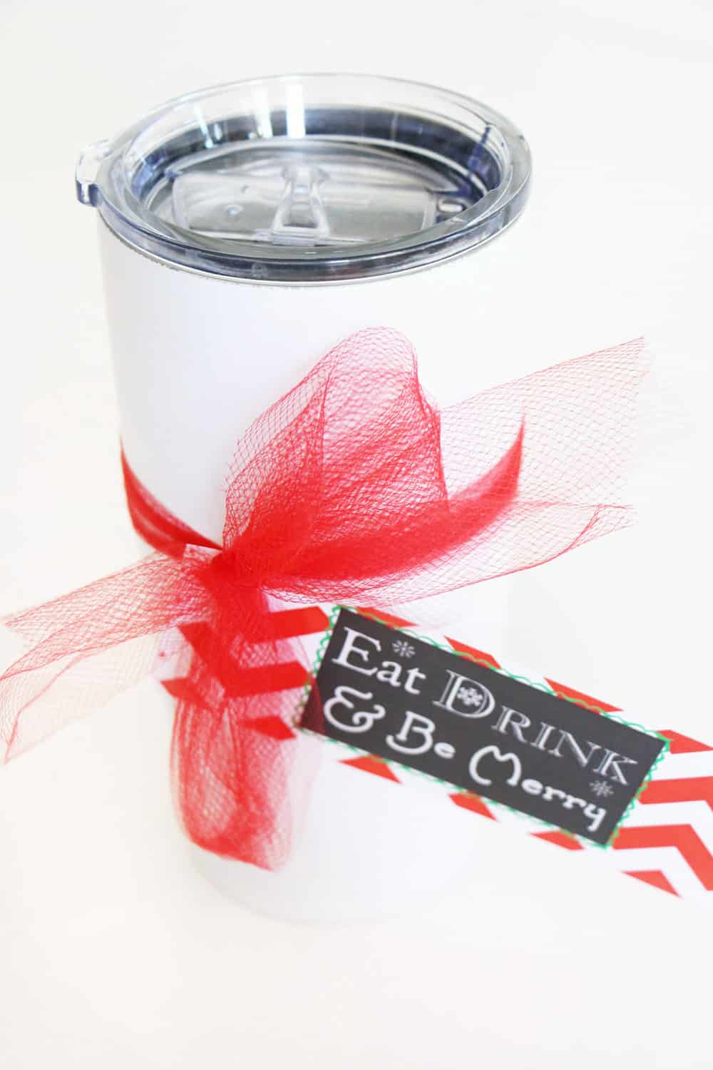 white tumbler with Christmas tag and red ribbon against a white background