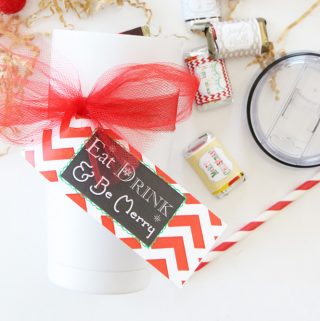 white tumbler with christmas tag on white counter with red and white straw, candy bars and brown crinkle papers