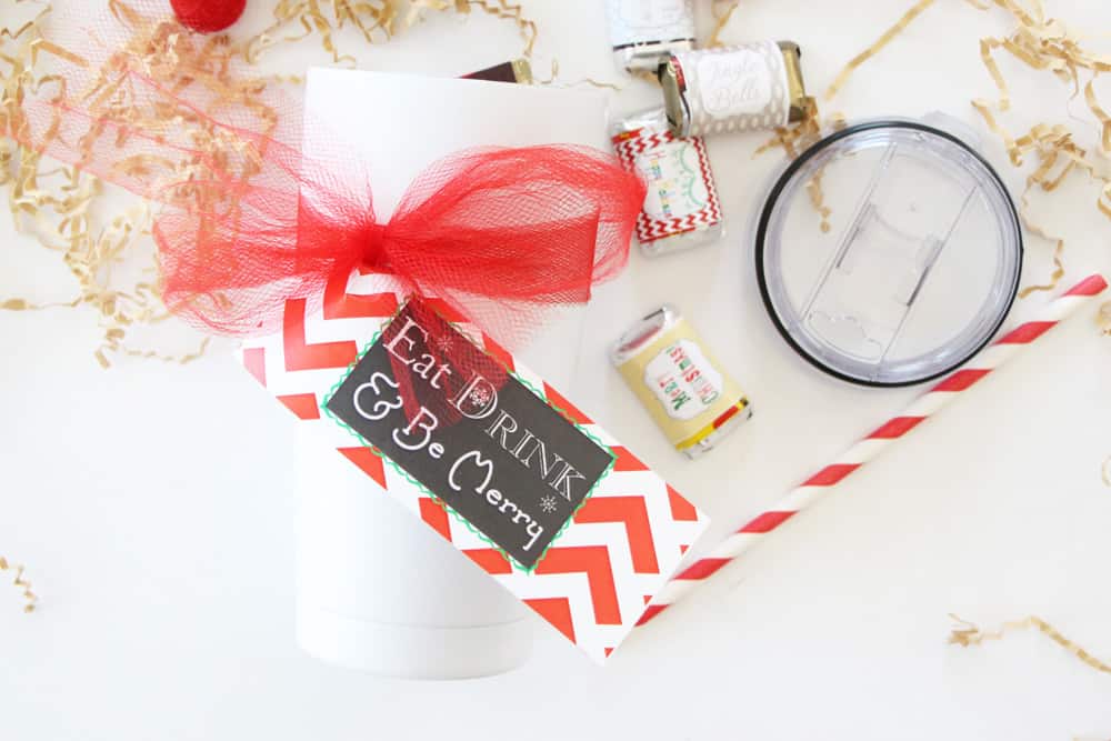 white tumbler with christmas tag on white counter with red and white straw, candy bars and brown crinkle papers