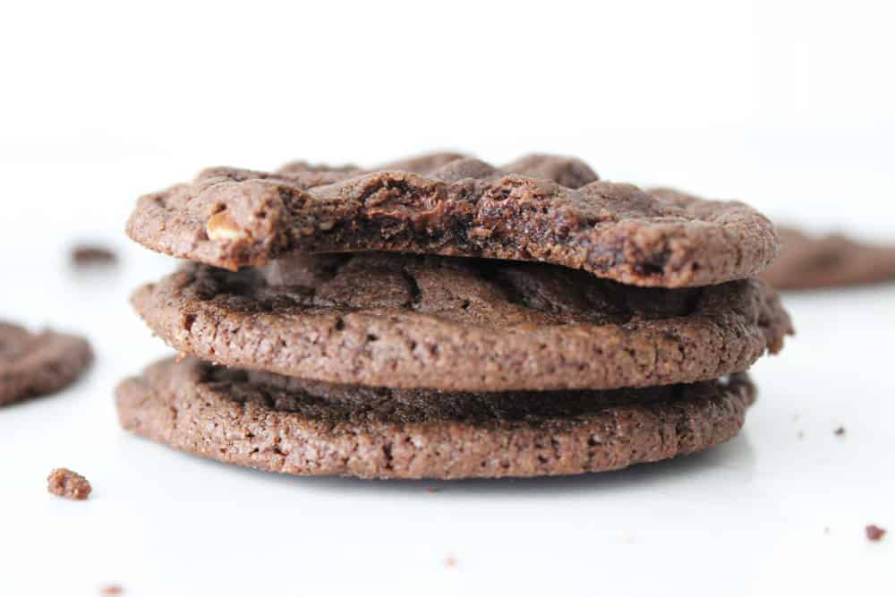 Three stacked double chocolate chip cookies on a white counter