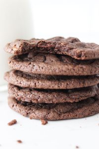 Stack of double chocolate chip cookies in front of a glass of milk on a white counter