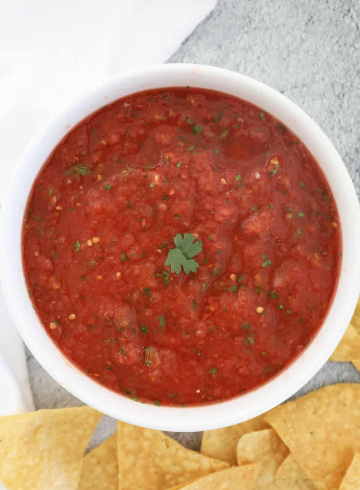 Blender salsa in a white bowl with tortilla chips underneath. 