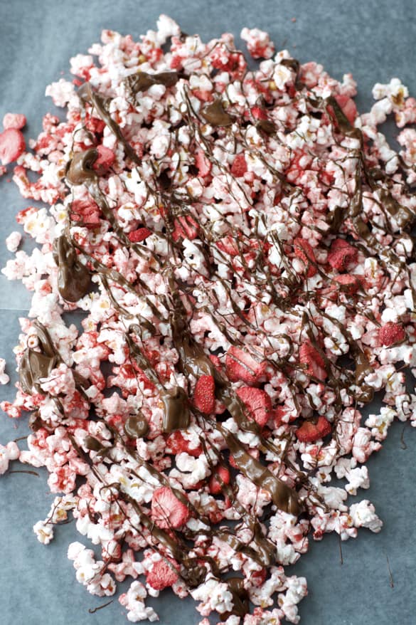 Chocolate Covered Strawberry Popcorn, pink popcorn with freeze dried strawberries covered in dark chocolate drizzle resting on parchment paper