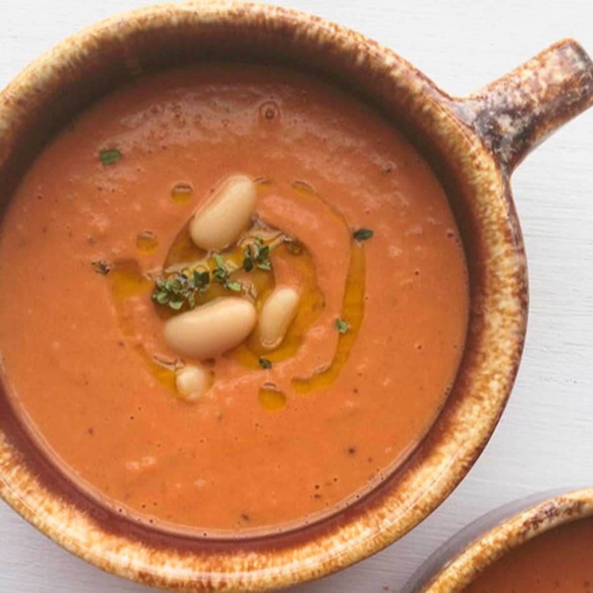 Tomato and White bean soup in a rustic bowl with thyme and white beans on top as a garnish.